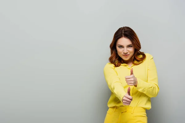 Femme joyeuse montrant pouces levés tout en souriant à la caméra sur gris — Photo de stock