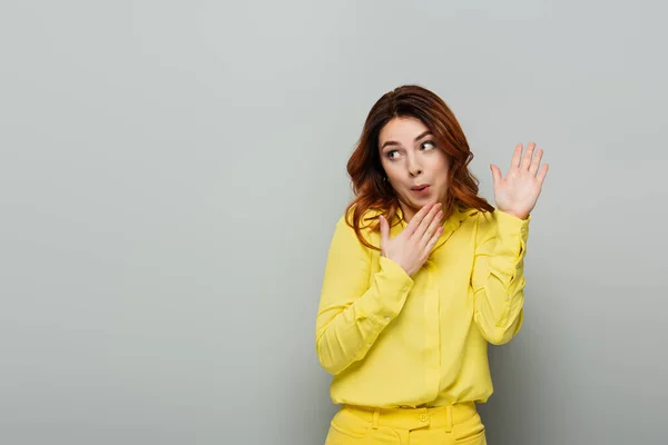 Confused woman pointing with hands while looking away on grey — Stock Photo