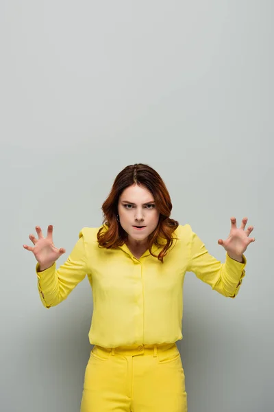 Сердитая женщина в жёлтой рубашке смотрит в камеру и показывает пугающий жест на сером — стоковое фото