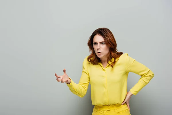 Сердита жінка показує лякаючий жест, стоячи з рукою на стегні на сірому — стокове фото