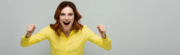 Excited woman showing success gesture while standing with open mouth isolated on grey, banner — Stock Photo