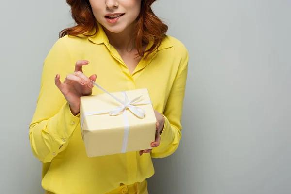 Partial view of coquettish woman opening gift box on grey — Stock Photo