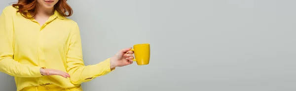 Vue partielle de la femme pointant vers la tasse jaune sur gris, bannière — Photo de stock