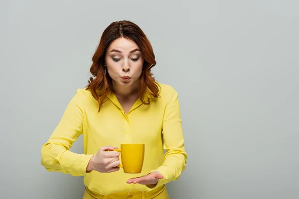 Femme choquée en chemisier jaune tenant tasse de thé chaud sur gris — Photo de stock