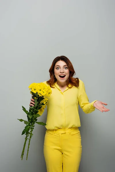 Erstaunte Frau mit gelben Blumen, während sie mit offenem Mund auf grau steht — Stockfoto