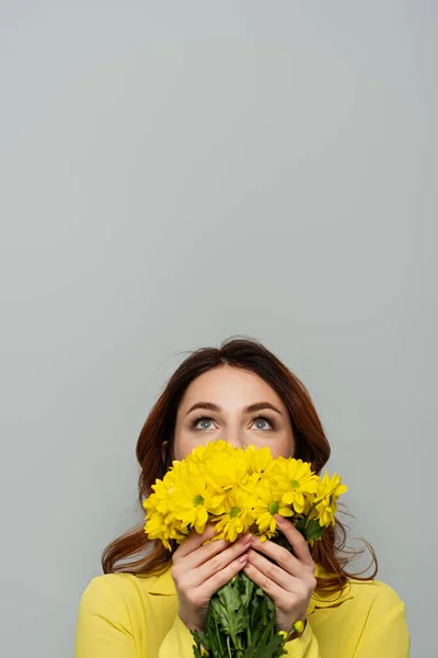Pleased woman looking up while obscuring face with yellow flowers isolated on grey — Stock Photo