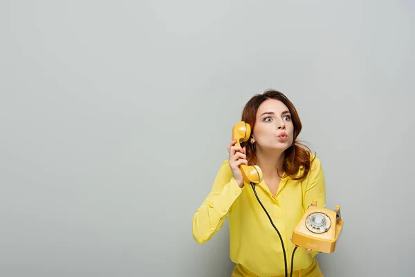 Überraschte Frau schmollt Lippen, während sie am Telefon auf grau spricht — Stockfoto