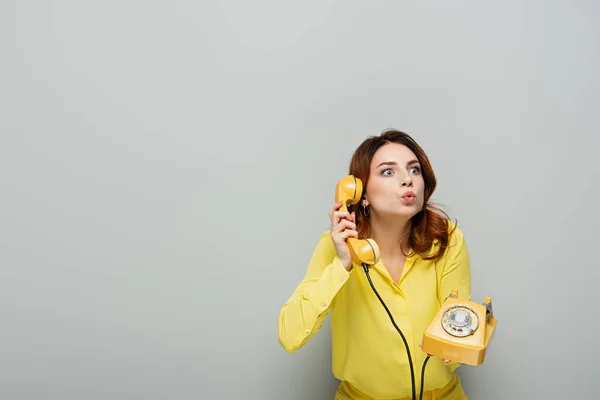 Femme surprise boudant lèvres tout en parlant sur téléphone vintage sur gris — Photo de stock