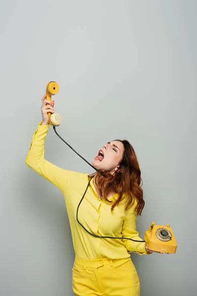 Femme se sentant dégoûté et sortant la langue tout en parlant téléphone vintage sur gris — Photo de stock