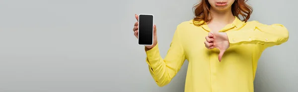 Teilansicht einer unzufriedenen Frau, die Abneigung zeigt, während sie ihr Smartphone mit leerem Bildschirm auf grau hält, Banner — Stockfoto