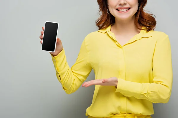 Abgeschnittene Ansicht einer lächelnden Frau, die auf ihr Handy zeigt, mit leerem Bildschirm auf grau — Stockfoto