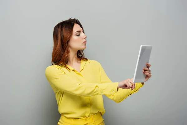 Ernsthafte Frau in gelber Bluse mit digitalem Tablet mit leerem Bildschirm auf grau — Stockfoto