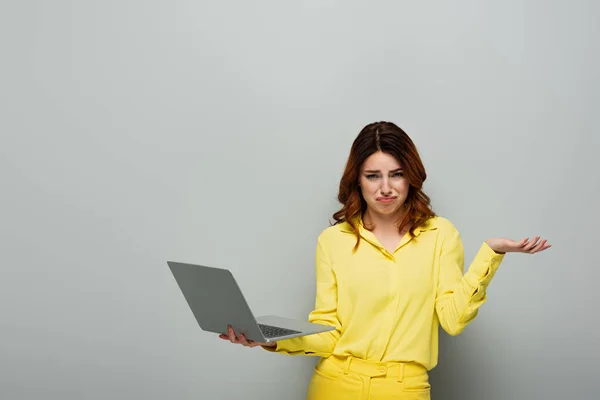 Upset woman looking at camera while holding laptop on grey — Stock Photo