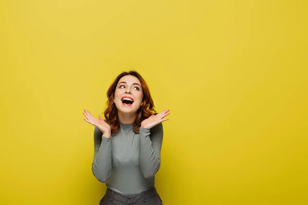 Mujer feliz con el pelo ondulado mirando hacia otro lado mientras está de pie con las palmas abiertas en amarillo - foto de stock