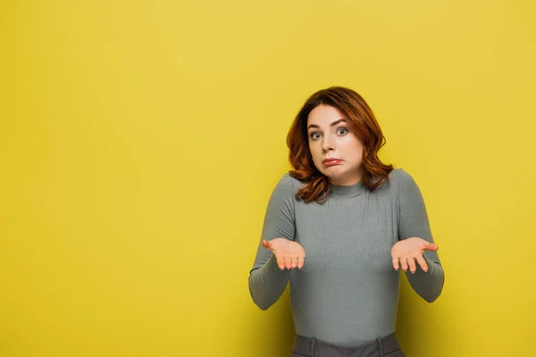 Confused woman pointing with hands while looking at camera on yellow — Stock Photo