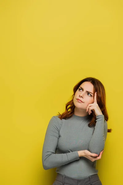 Worried woman touching head and looking away while thinking on yellow — Stock Photo
