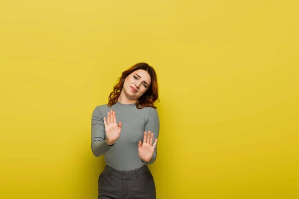 Dissatisfied woman looking at camera while showing stop gesture on yellow — Stock Photo