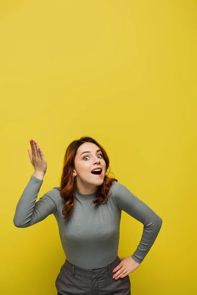 Thrilled woman looking at camera while standing with hand on hip and pointing with hand on yellow — Stock Photo