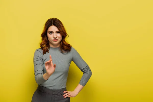Незадоволена жінка стоїть з рукою на стегні і вказує пальцем, не показуючи ніякої ознаки на жовтому — стокове фото