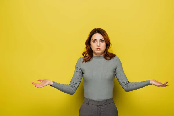 Confused young woman with curly hair showing shrug gesture on yellow — Stock Photo