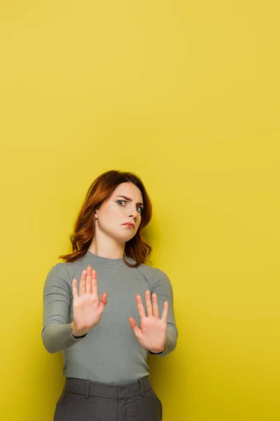 Mujer disgustada con el pelo ondulado mostrando gesto de parada y mirando a la cámara en amarillo - foto de stock