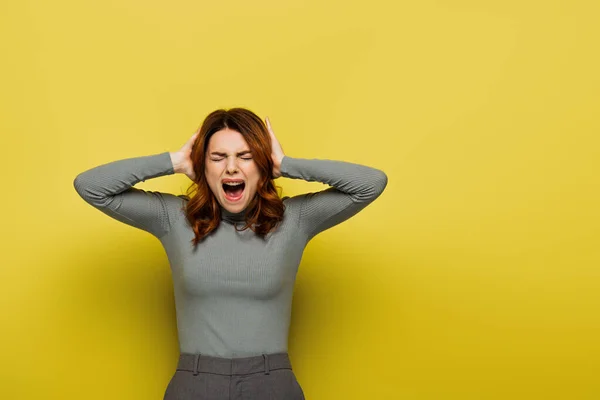 Mujer joven gritando mientras toca la cabeza en amarillo - foto de stock