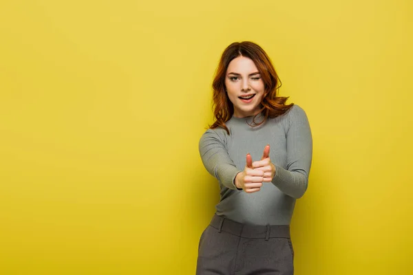 Mujer alegre con el pelo rizado mostrando los pulgares hacia arriba en amarillo - foto de stock