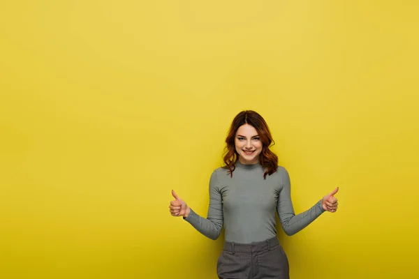 Mujer feliz con el pelo rizado mostrando los pulgares hacia arriba en amarillo - foto de stock