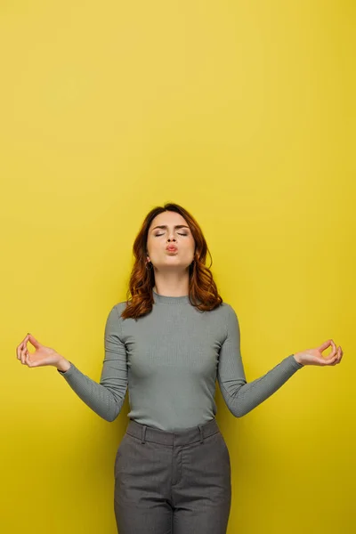 Mujer con el pelo rizado y los ojos cerrados hinchando mejillas mientras medita en amarillo - foto de stock