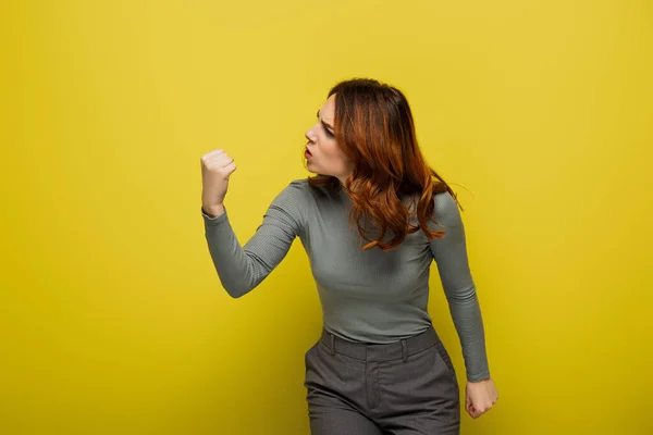 Donna arrabbiata con i capelli ricci mostrando pugno serrato sul giallo — Foto stock