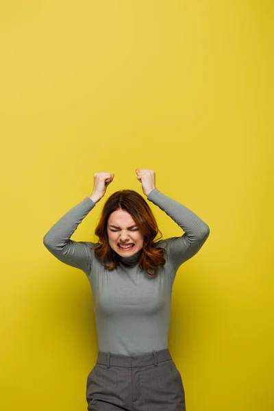 Mujer irritada con el pelo ondulado y los ojos cerrados de pie con los puños apretados en amarillo - foto de stock