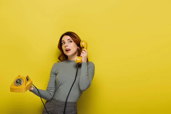 Junge Frau streckt Zunge heraus, während sie Retro-Telefon auf gelb hält — Stockfoto
