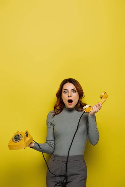 Schockierte junge Frau hält Retro-Telefon isoliert auf gelb — Stockfoto