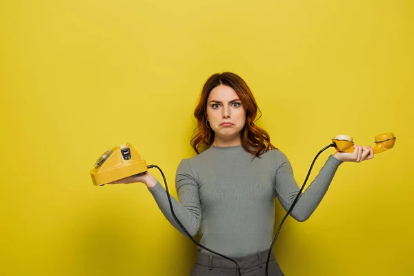 Traurige junge Frau hält Retro-Telefon auf gelb — Stockfoto