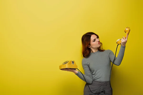 Unzufriedene junge Frau schaut auf Retro-Handy in Gelb — Stockfoto