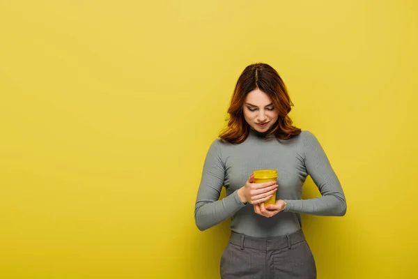 Junge Frau mit lockigem Haar hält Pappbecher auf gelb — Stockfoto