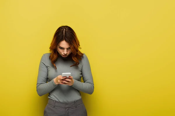 Jeune femme avec des messages de cheveux bouclés sur téléphone mobile sur jaune — Photo de stock