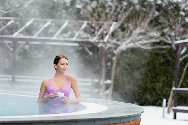 Fröhliche junge Frau im Badeanzug mit einer Tasse Kaffee im Freibad — Stockfoto