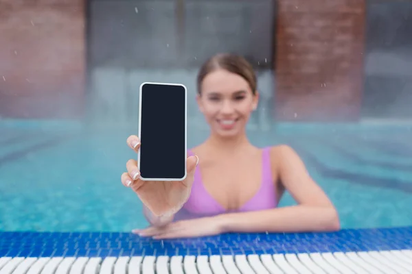 Verschwommene und glückliche Frau hält Smartphone mit leerem Bildschirm beim Baden im Freibad — Stockfoto