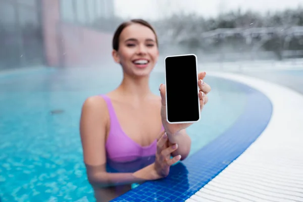 Donna allegra che tiene smartphone con schermo bianco mentre fa il bagno nella piscina all'aperto — Foto stock