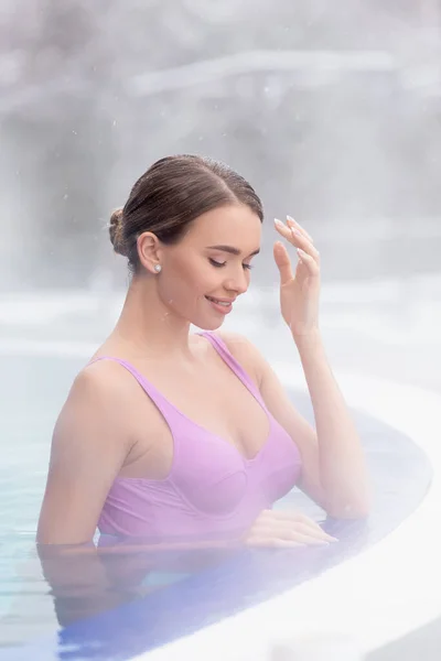 Vapeur près de sourire jeune femme se baignant dans la piscine extérieure de source chaude — Photo de stock