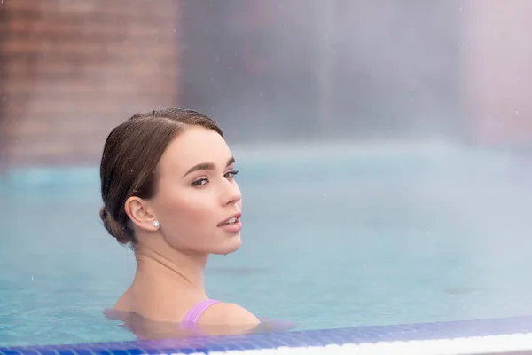 Jeune femme regardant loin et prenant un bain dans la piscine extérieure de source chaude — Photo de stock