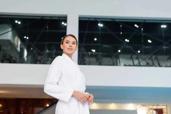 Lächelnde junge Frau im weißen Bademantel steht im Wellness-Center — Stockfoto