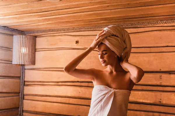 Giovane donna asciugamano di fissaggio sulla testa in sauna — Foto stock