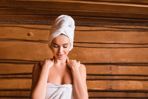 Donna sorridente che si tiene per mano sulle spalle in sauna di legno su sfondo sfocato — Foto stock