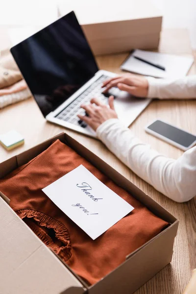 Partial view of showroom owner working near box with clothes and card with thank you lettering, blurred background — Stock Photo