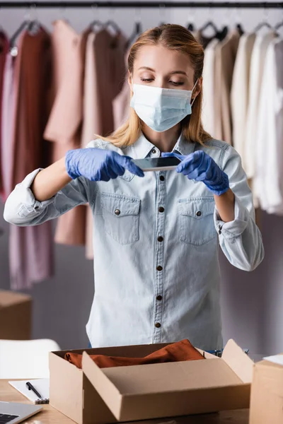 Propriétaire en masque médical, prendre une photo de la boîte avec des vêtements dans la salle d'exposition — Photo de stock