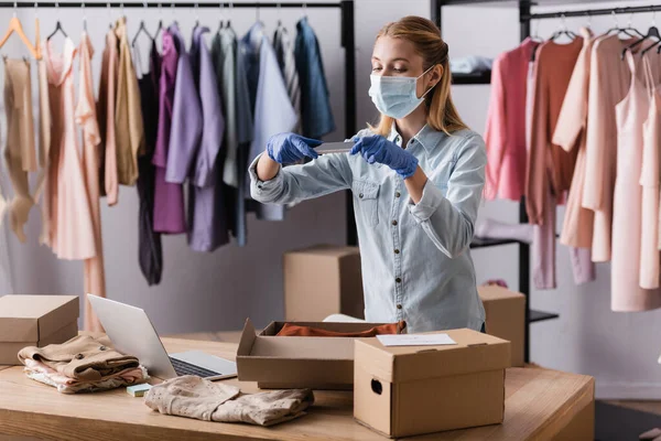 Young showroom owner in protective mask, taking photo of cardboard boxes at workplace — Stock Photo