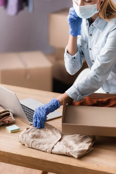 Partial view of proprietor in medical mask, packing clothes into box in showroom — Stock Photo
