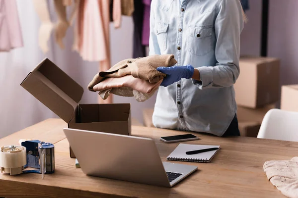 Partial view of proprietor in latex glove packing clothes into box in showroom — Stock Photo